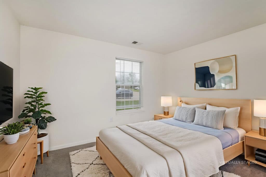 Bedroom with a wooden bed, blue and white bedding, two lamps, a dresser with plants, a large window, and abstract art on the wall.