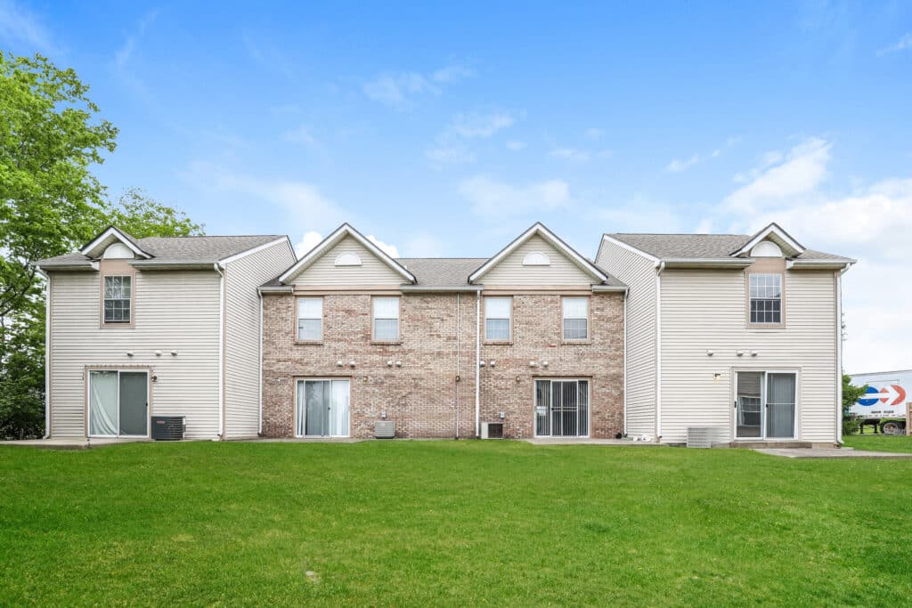 Two-story brick and siding townhouse building with three entrances, large windows, and a green lawn in the foreground under a clear blue sky.