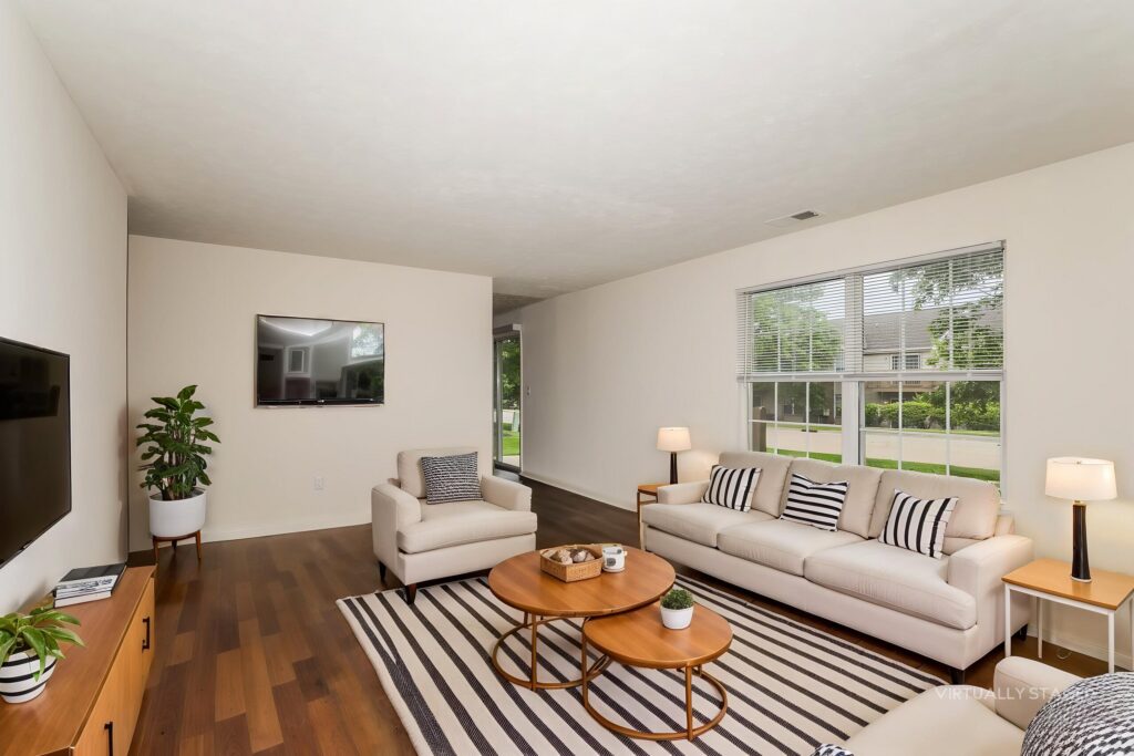 Modern living room with hardwood floors, beige walls, a white sofa, striped rug, round wooden coffee tables, armchair, flat-screen TV, potted plant, and large window letting in natural light.
