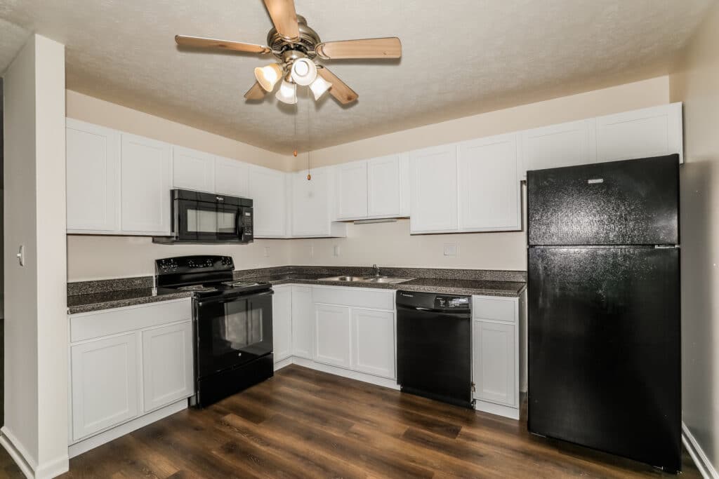 Modern kitchen with white cabinets, black appliances including fridge, stove, microwave, and dishwasher, wood-style flooring, and a ceiling fan with lights.