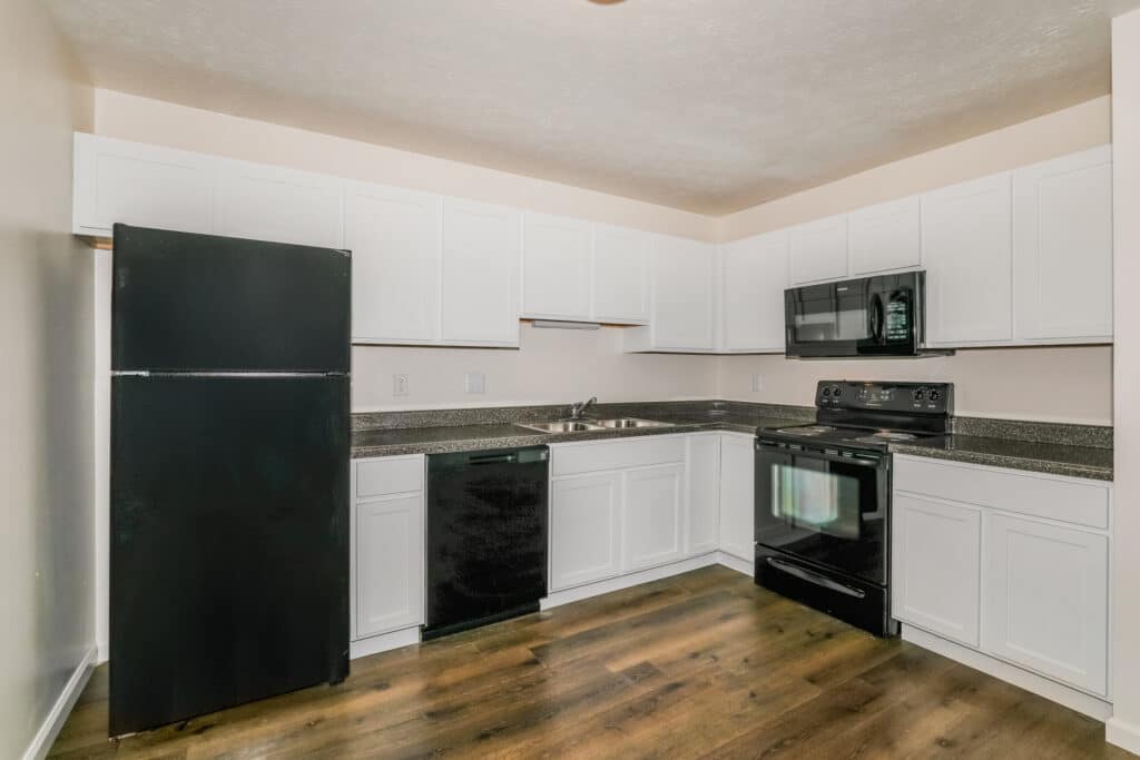 Modern kitchen with white cabinets, black appliances including a refrigerator, dishwasher, stove, and microwave, and wood-style flooring.