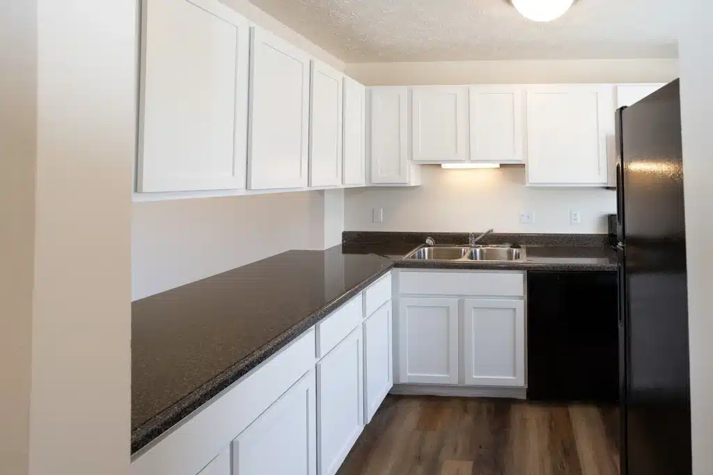 Modern kitchen with white cabinets, black appliances, double sink, dark countertops, and wood-look flooring.