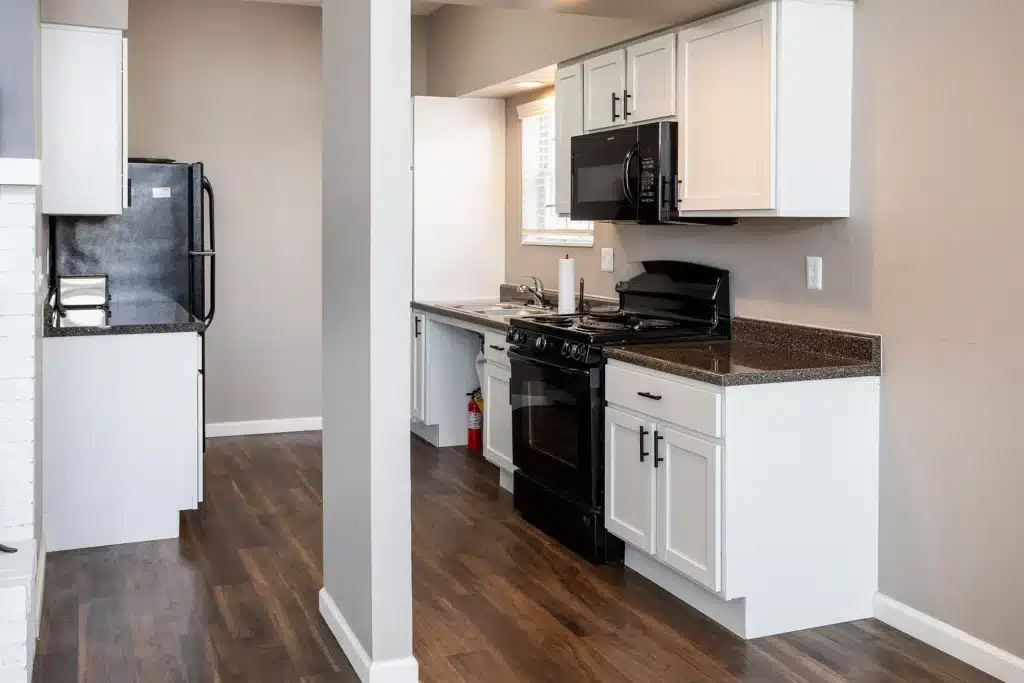 Modern kitchen with white cabinets, black appliances, dark countertops, wood flooring, and a fire extinguisher near the sink.